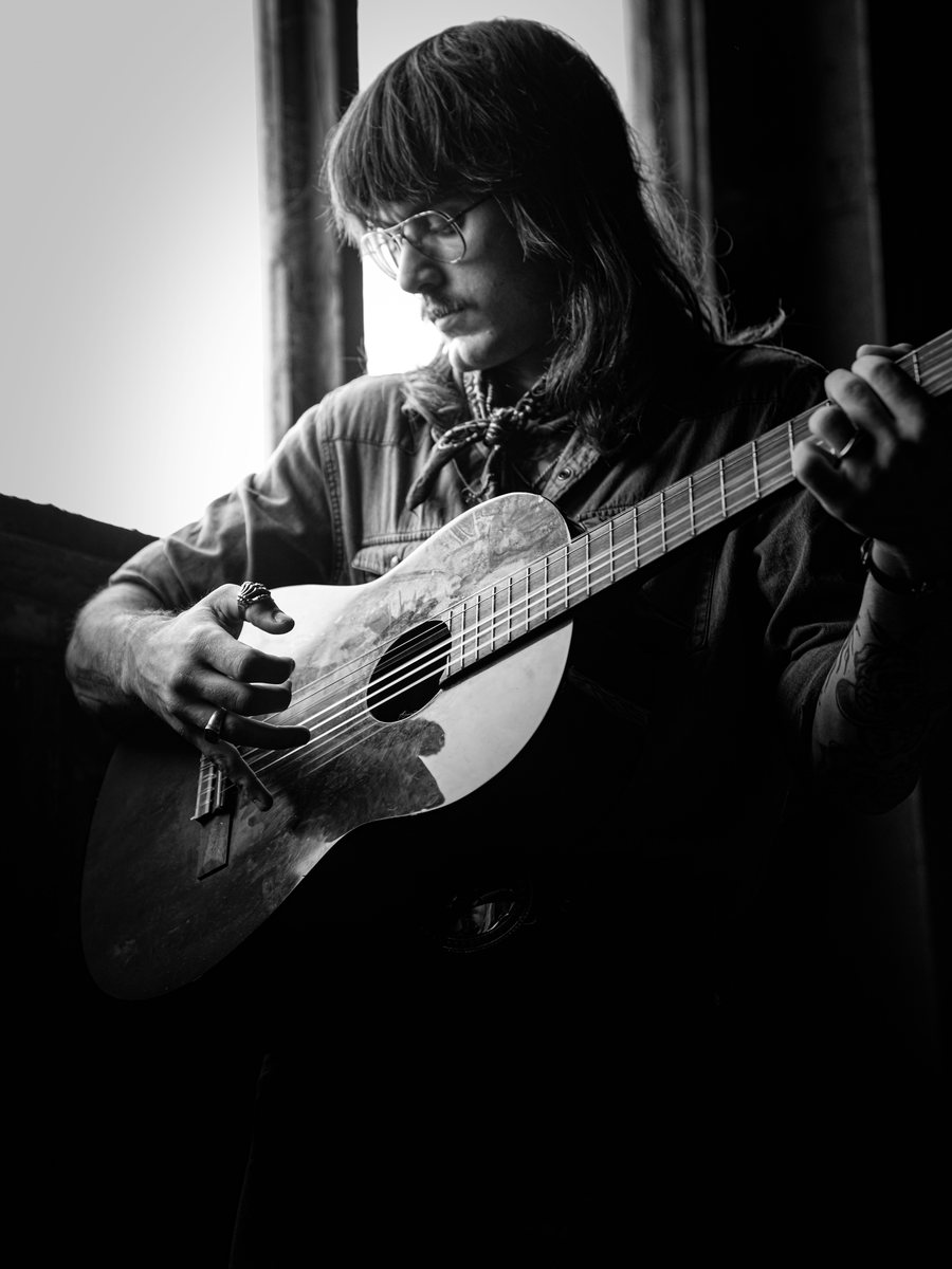 Vertical portrait playing the parlor guitar by a window