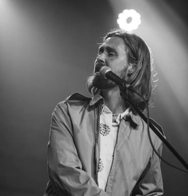 Tobias Lund singing at the keys under a stage light, in black and white